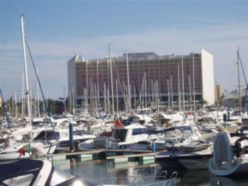 Puerto deportivo con muchos yates y barcos amarrados en el muelle, frente a un edificio de varios pisos.