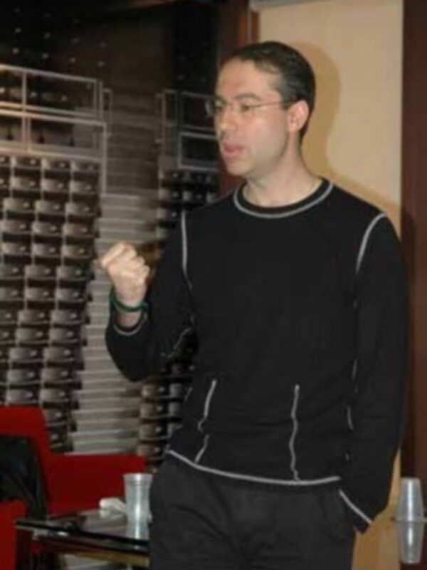 Un hombre con gafas y una camiseta negra está en un entorno de oficina, posiblemente durante una presentación o conferencia.