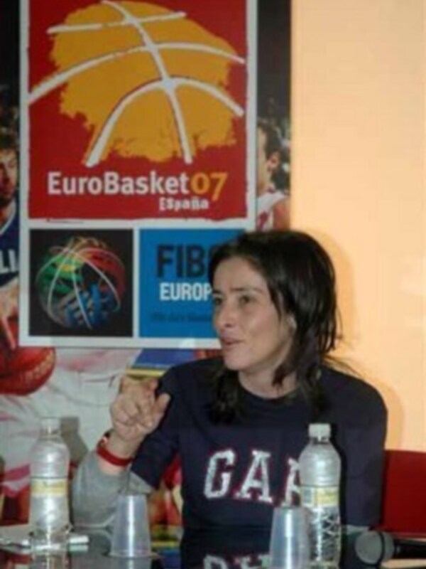 Una mujer habla en una conferencia de prensa con un cartel del EuroBasket 2007 y el logo de la FIBA en el fondo.