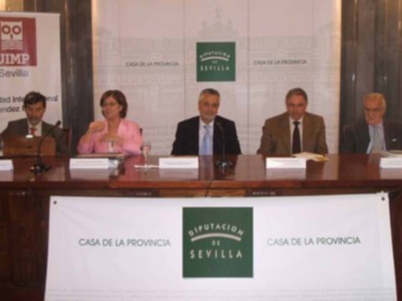 Una conferencia de prensa en la Casa de la Provincia de Sevilla, con varios oradores sentados en una mesa. El fondo muestra banners de la UIMP y la Casa de la Provincia de Sevilla.