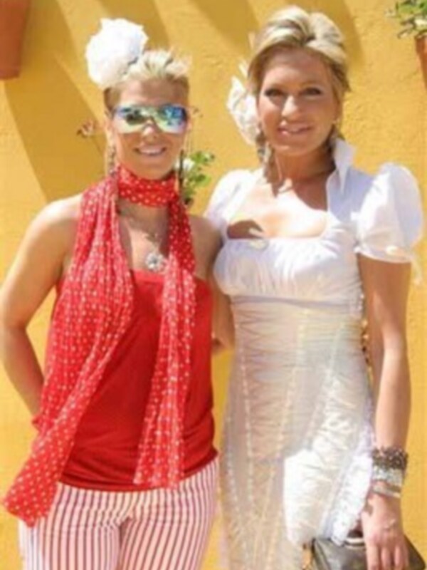 Dos personas vestidas con ropa de verano, una con una blusa roja y el otro con una blusa blanca, posando frente a una pared amarilla.