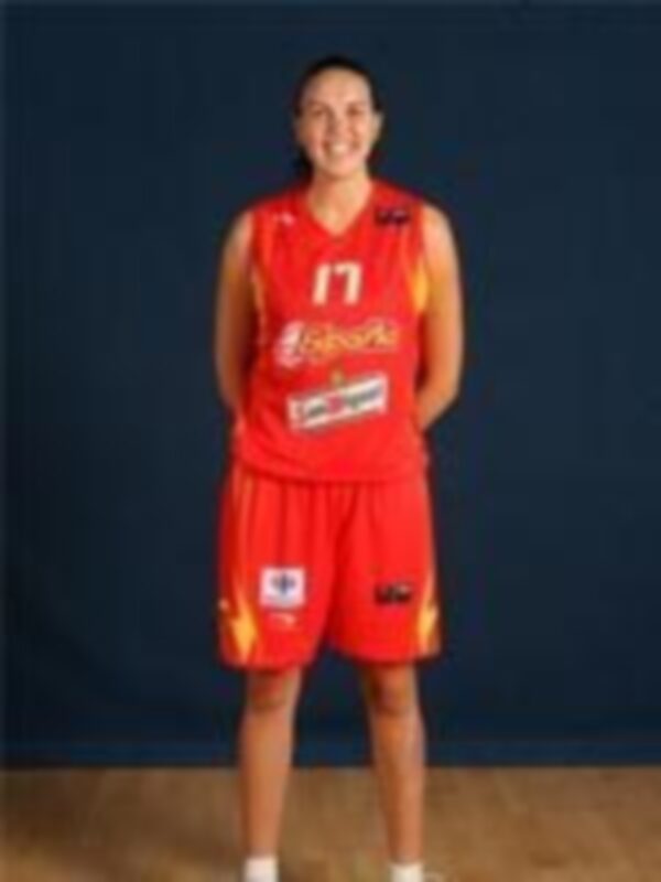 Una mujer vestida con un uniforme de baloncesto rojo y amarillo, posando frente a una pared blanca.