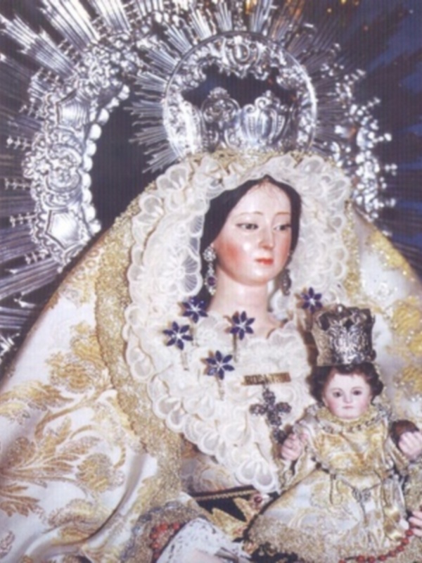 Imagen de una Virgen con niño en sus brazos, vestida con trajes dorados y adornos florales.