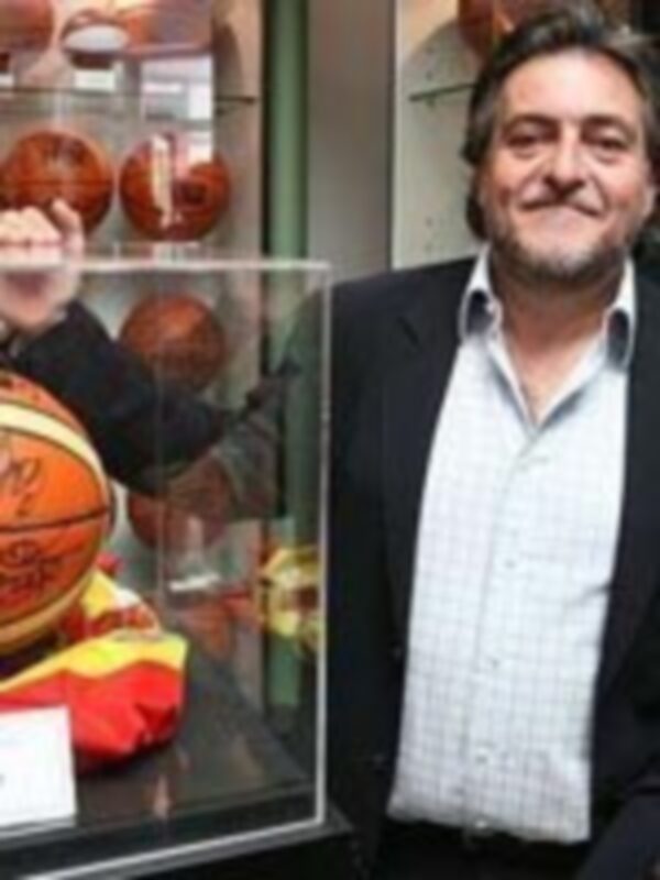 Un hombre sonríe mientras sostiene una pelota de baloncesto en un escaparate. La imagen parece ser parte de una campaña publicitaria o promocional relacionada con el deporte.
