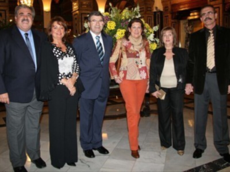 Grupo de personas en un evento formal, posando frente a una decoración floral.