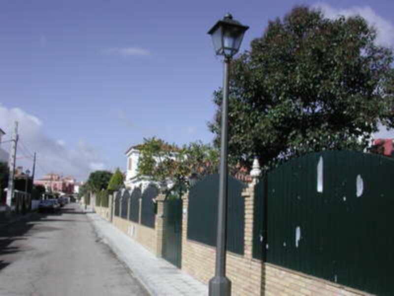 Un camino asfaltado bordeado de una cerca de ladrillo y un árbol en el fondo.