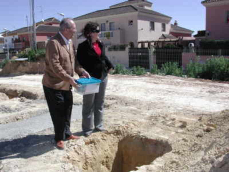 Dos personas observan una excavación en terreno baldío, posiblemente un proyecto de construcción.