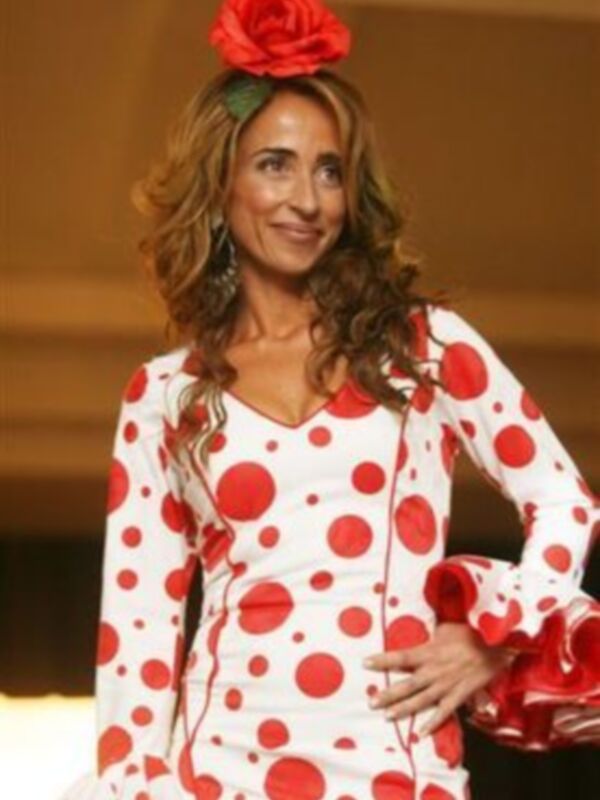 Una mujer con vestido de flamenco blanco y rojo, lleva un tocado floral rojo en su cabeza.