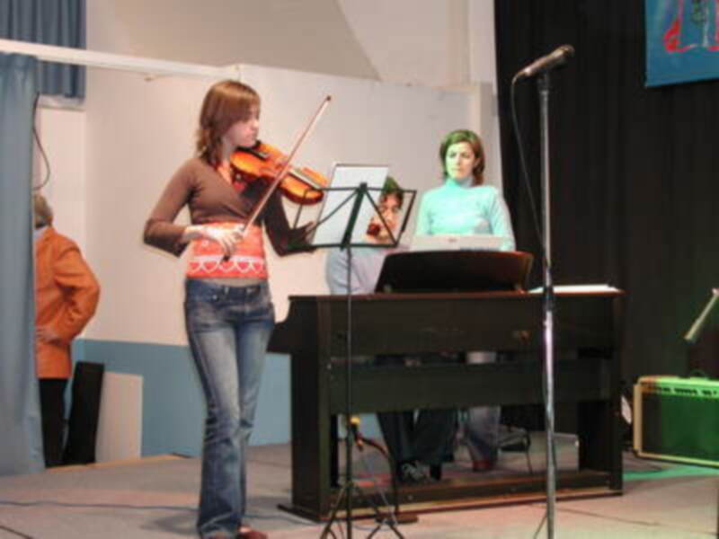 Una joven violinista en el centro de la imagen, con un violín y un piano al lado.