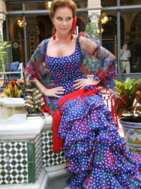 Elegante mujer en vestido de flamenco sentada en un patio decorado con plantas y detalles moriscos.