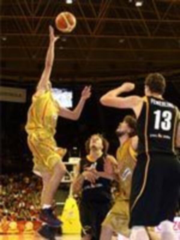 Un jugador de baloncesto en amarillo realiza un tiro libre mientras otros jugadores observan. El fondo muestra una cancha de baloncesto con espectadores en el estadio.