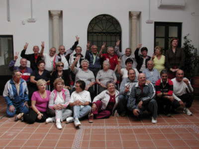 Grupo de personas mayores posando juntos en un interior con ventanas arqueadas.