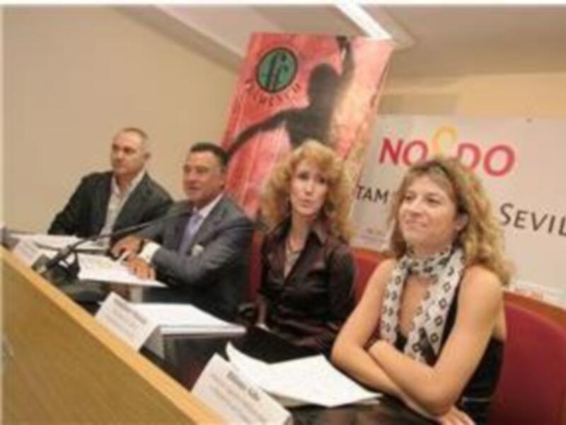 Una reunión formal en Sevilla, con personas sentadas en una mesa y una bandera de Sevilla en el fondo.