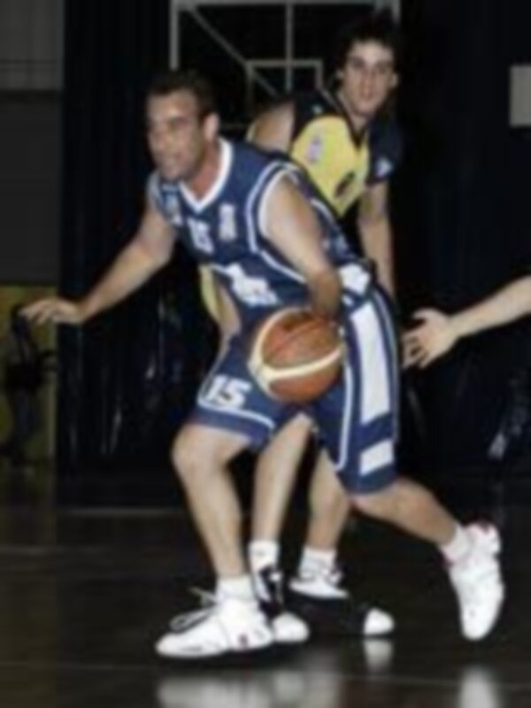 Un jugador de baloncesto en acción durante un partido, con el balón en la mano y otros jugadores en el fondo.