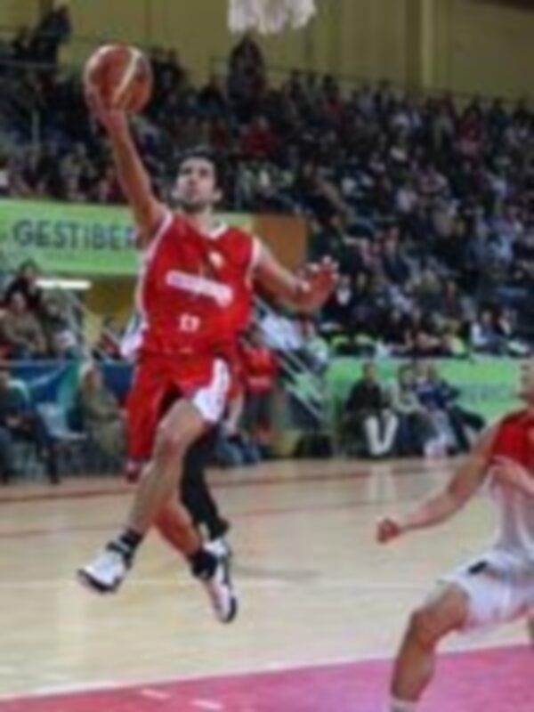 Un jugador de baloncesto en acción, lanzando el balón en un partido de baloncesto en un estadio lleno de espectadores.