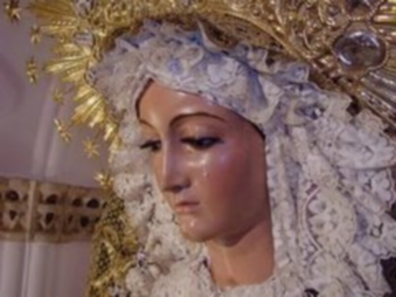 Una imagen de una Virgen María vestida con trajes tradicionales y adornos religiosos, posiblemente en una celebración religiosa o procesión.