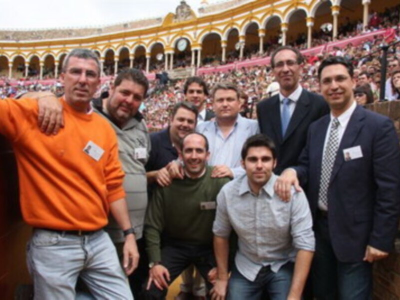 Grupo de personas posando en un estadio lleno, con una torre amarilla y roja al fondo.