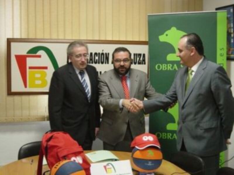 Tres personas en trajes estrechando manos en una reunión, con un letrero de la empresa F.B. en el fondo.