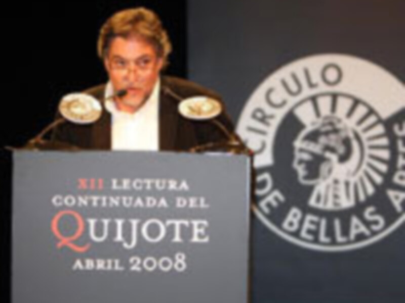 A una persona en un evento de lectura del Quijote, celebrado en el Círculo de Bellas Artes en abril de 2008. La persona está detrás de un micrófono, con una pantalla que dice "Serie Lectura Continuada del Quijote Abril 2008".