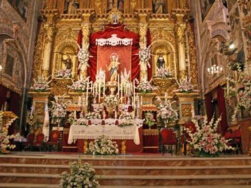 Interior de una iglesia con altares dorados, flores y decoraciones.