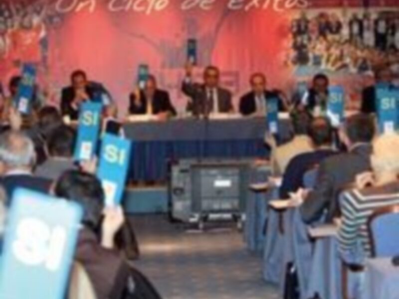 Una conferencia o evento con varios presentadores sentados en un escenario, sosteniendo carteles con texto. La imagen muestra una atmósfera formal y profesional.