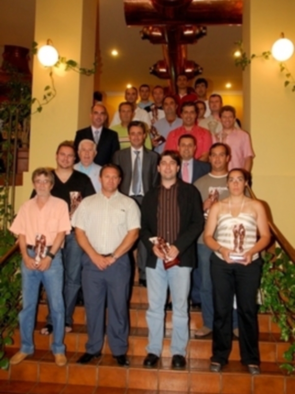 Una reunión de equipo en un ambiente formal, con una persona sosteniendo un trofeo. La imagen muestra a varias personas en trajes y camisas, posiblemente celebrando un logro. La decoración incluye plantas y luces, creando una atmósfera festiva.