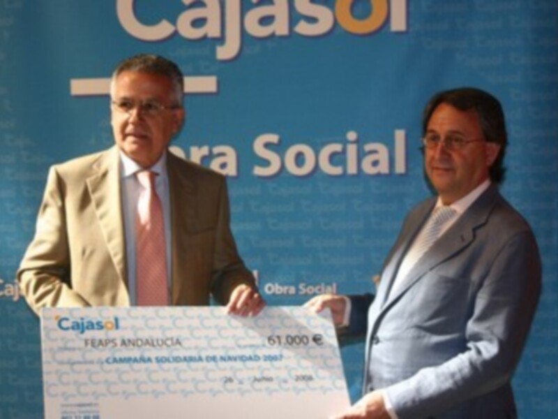 Dos hombres sostienen un gran cheque de 61.000 euros en una conferencia de prensa con el logo de Cajasol y la palabra "Campaña Social".