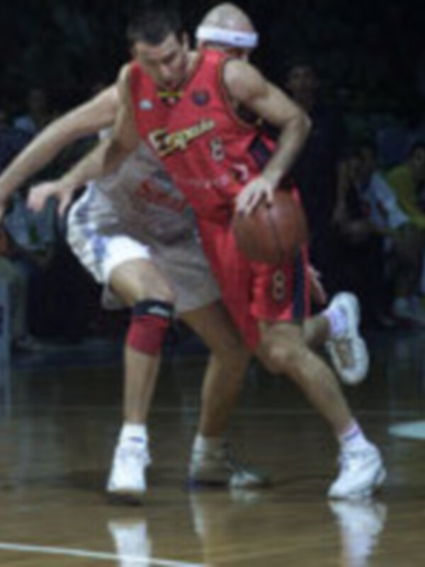 Un jugador de baloncesto en acción durante un partido, con una camiseta roja y blanco y una gorra blanca.