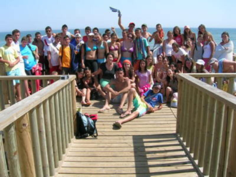 Grup de persones a la platja, amb una vista del mar i un sol brillant.
