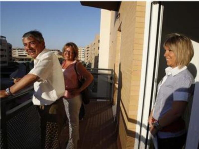 Tres personas sonrientes en una terraza con vistas al mar, en un día soleado.