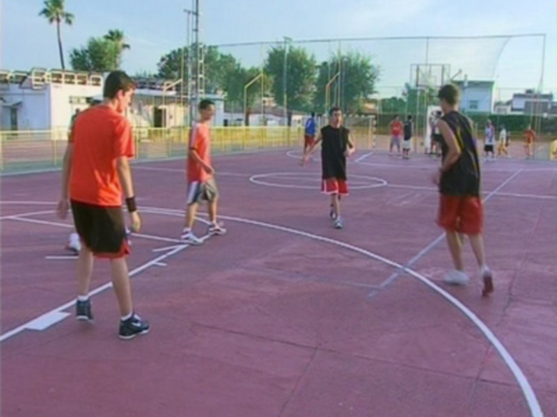Jóvenes jugando baloncesto en una cancha de deporte al aire libre.
