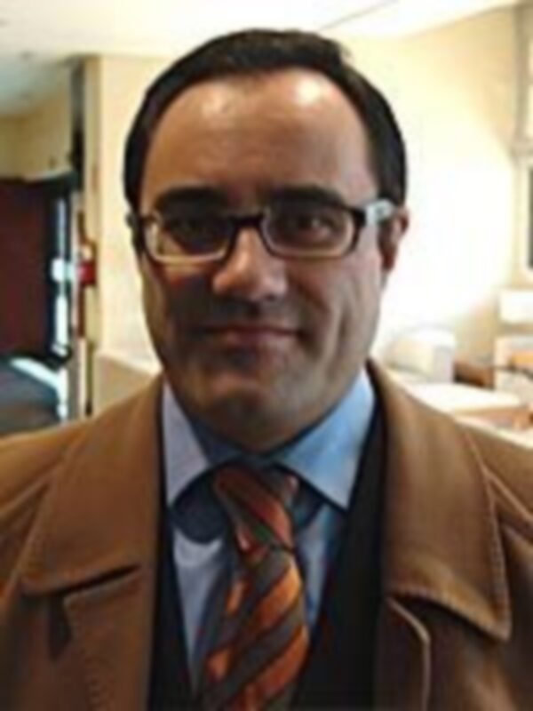 Un hombre con una chaqueta de color beige y un cuello naranja, posiblemente en una oficina o sala de conferencias.