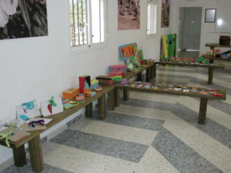 Un ambiente educativo con mesas de madera y libros, decorado con pinturas y plantillas en forma de frutas.