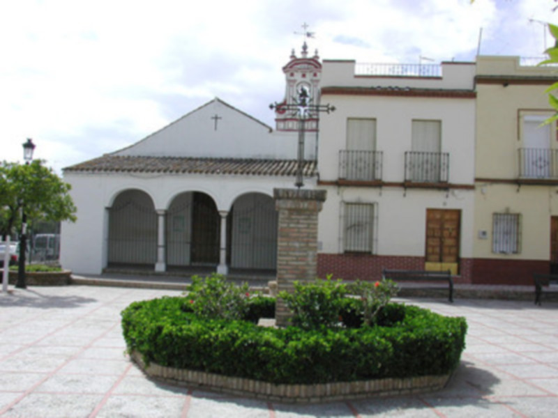 Un pequeño pueblo con una iglesia blanca y un pequeño parque con arbustos verdes en el centro.