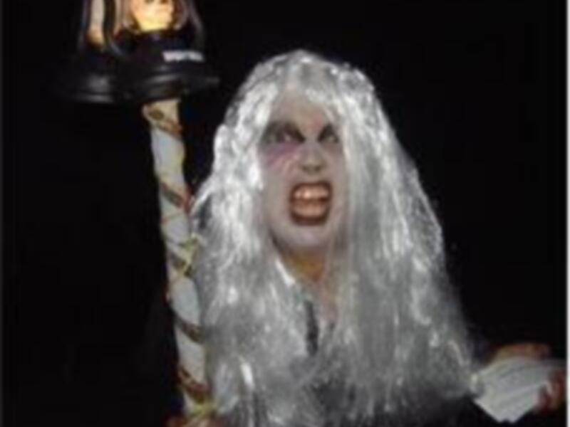 Una figura con cabello blanco y una máscara de terror sostiene una linterna con una figura en su interior, probablemente representando una escena de terror o miedo.