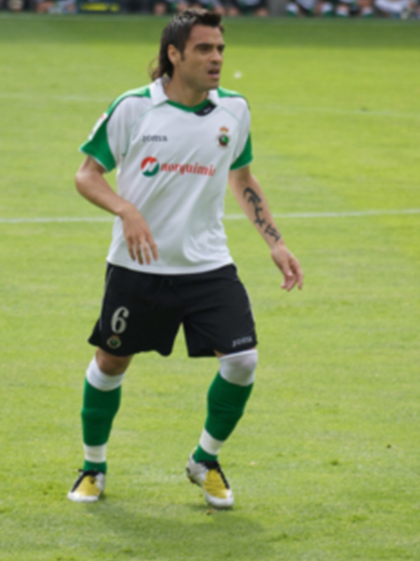 Jugador de fútbol en acción con uniforme blanco y verde, número 6 visible en la camiseta.