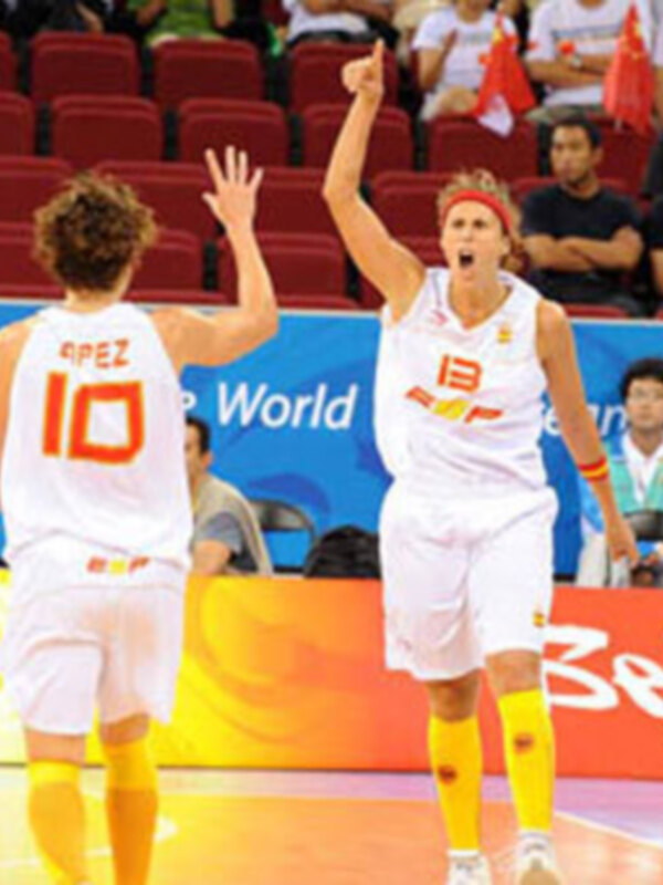 Dos jugadoras celebran en un partido de baloncesto, con el escudo del equipo visible. La imagen muestra una celebración emocionante en un estadio lleno de espectadores.