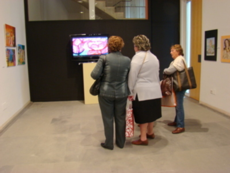 Tres personas observan una pantalla de televisión en un espacio con arte en las paredes.
