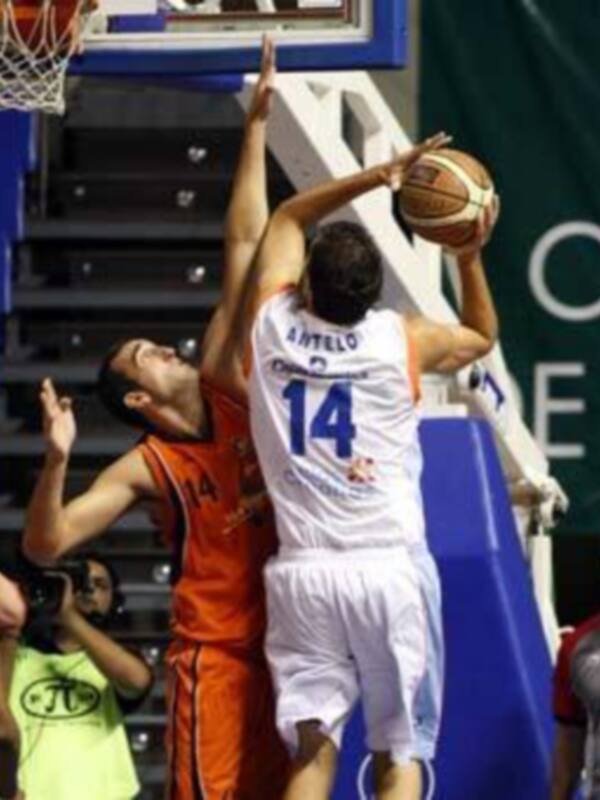 Jugador en blanco intenta anotar mientras un defensor en naranja intenta bloquear durante un partido de baloncesto.