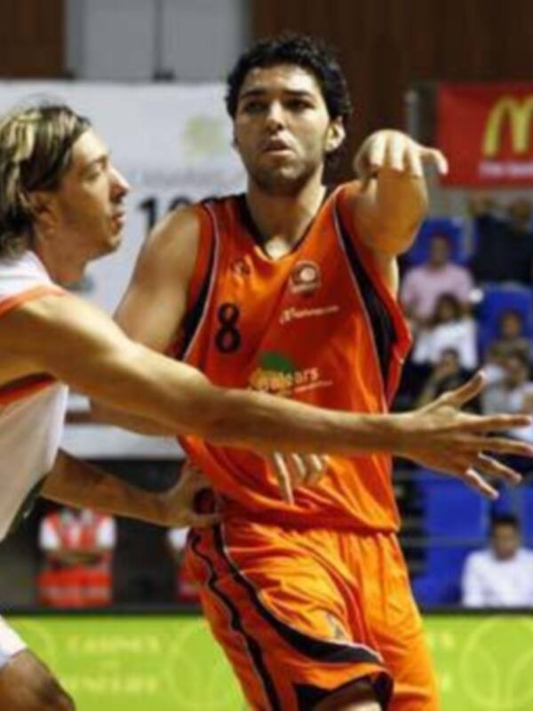 Un jugador de baloncesto en una camiseta naranja con el número 8 intenta un tiro libre mientras otro jugador en una camiseta blanca lo defiende. En el fondo, se pueden ver espectadores sentados en los asientos del estadio y una publicidad de McDonald's.