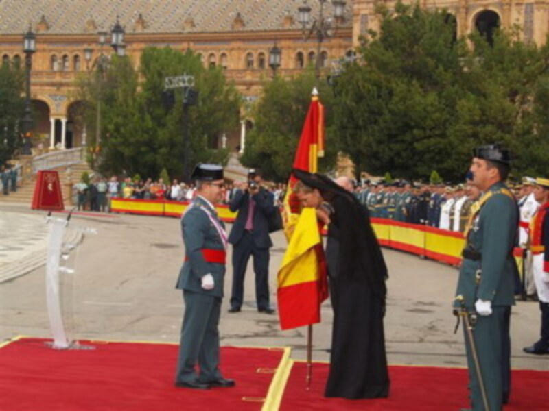 Ceremonia oficial en la Plaza de España de Sevilla, con uniformes militares y bandera española.