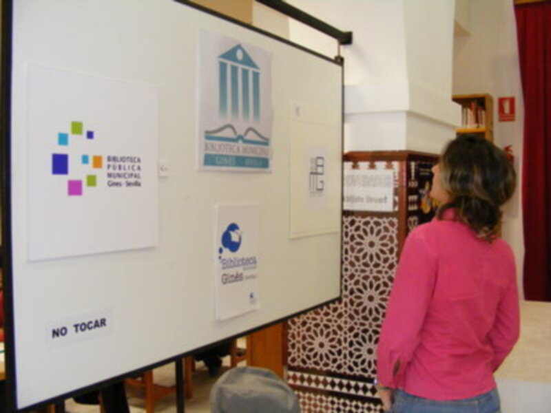 Una persona con una chaqueta rosa observa un panel informativo en la Biblioteca Municipal de Quito, con logos y texto que promueven actividades culturales.