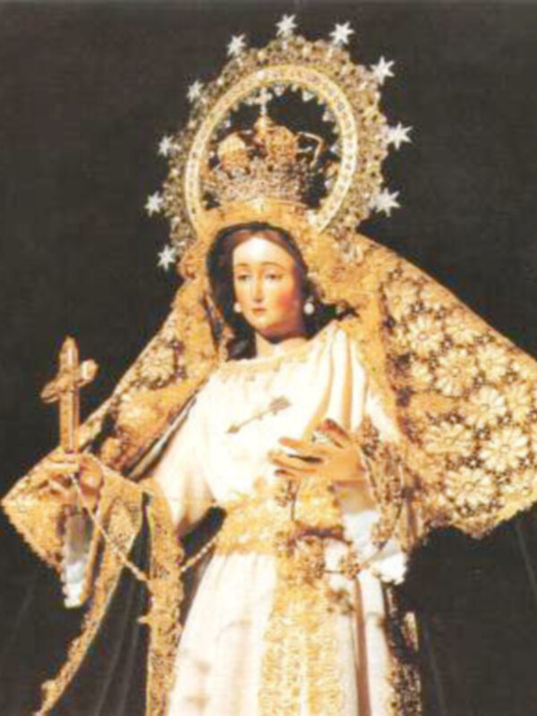 Una estatua de la Virgen María vestida con un manto dorado y una corona, sosteniendo un palo de mando. La escena es dramática y sagrada, típica de la devoción católica.