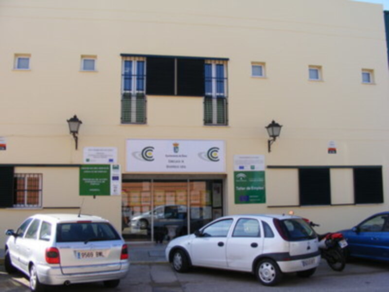 Fachada amarilla de un edificio con ventanas y puertas, dos coches estacionados y una motocicleta.