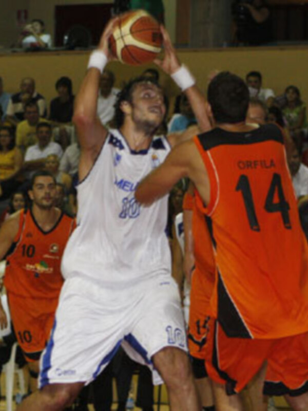 Jugadores de baloncesto en acción durante un partido, uno en blanco y otro en naranja, en un estadio lleno de espectadores.