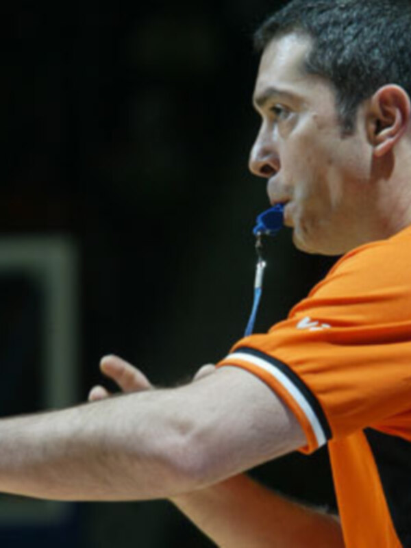 Árbitro de baloncesto en acción, sosteniendo un silbato y apuntando con el brazo.
