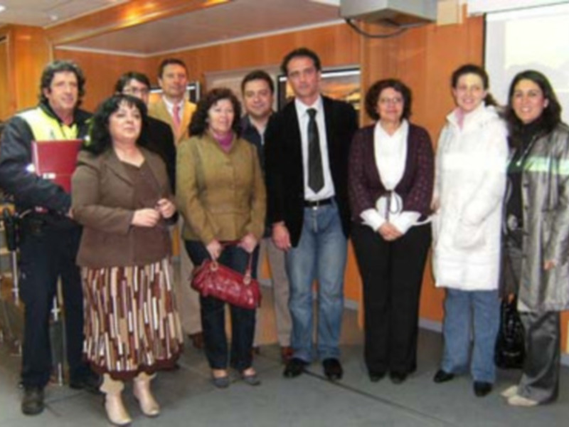 Una imagen de un grupo de siete personas posando juntos en una oficina. La persona central es un hombre con una camisa blanca y corbata, mientras que las demás personas son de diferentes edades y estilos. La imagen muestra una oficina con escritorios, un mostrador de recepción y una puerta al fondo.