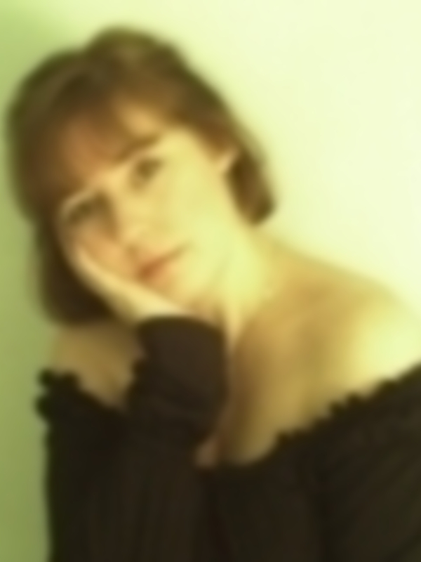 Una mujer con cabello largo y ondulado, vistiendo un vestido negro sin mangas. La imagen tiene una textura suave y el fondo es de color claro, probablemente blanco o beige.