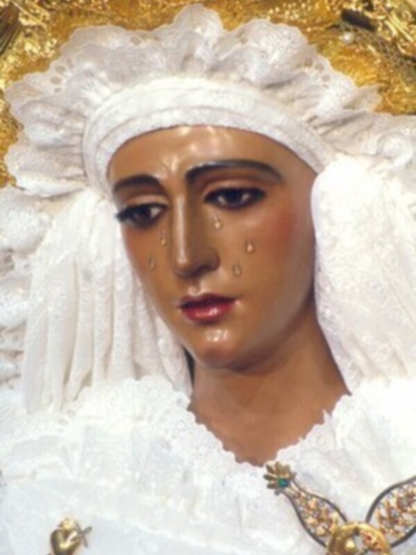 Imagen de la Virgen de la Soledad con vestimentas blancas y una corona dorada, representando tristeza y devoción.