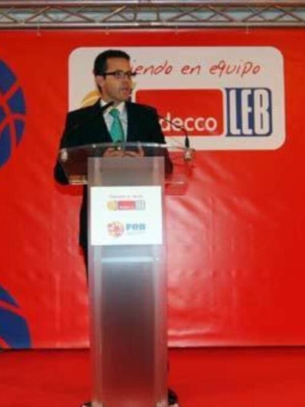 Un hombre en traje negro y corbata verde se encuentra al frente de un podio, en una conferencia o evento. El fondo es rojo con logos y texto que dice "endo en equipo" y "decco LEB".
